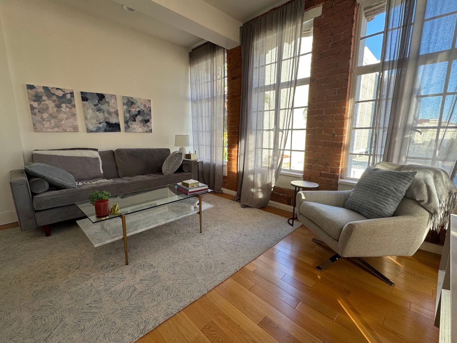 Sunlit therapy room with a gray sofa, armchair, and tall windows in Dr. Maya's Santa Monica office